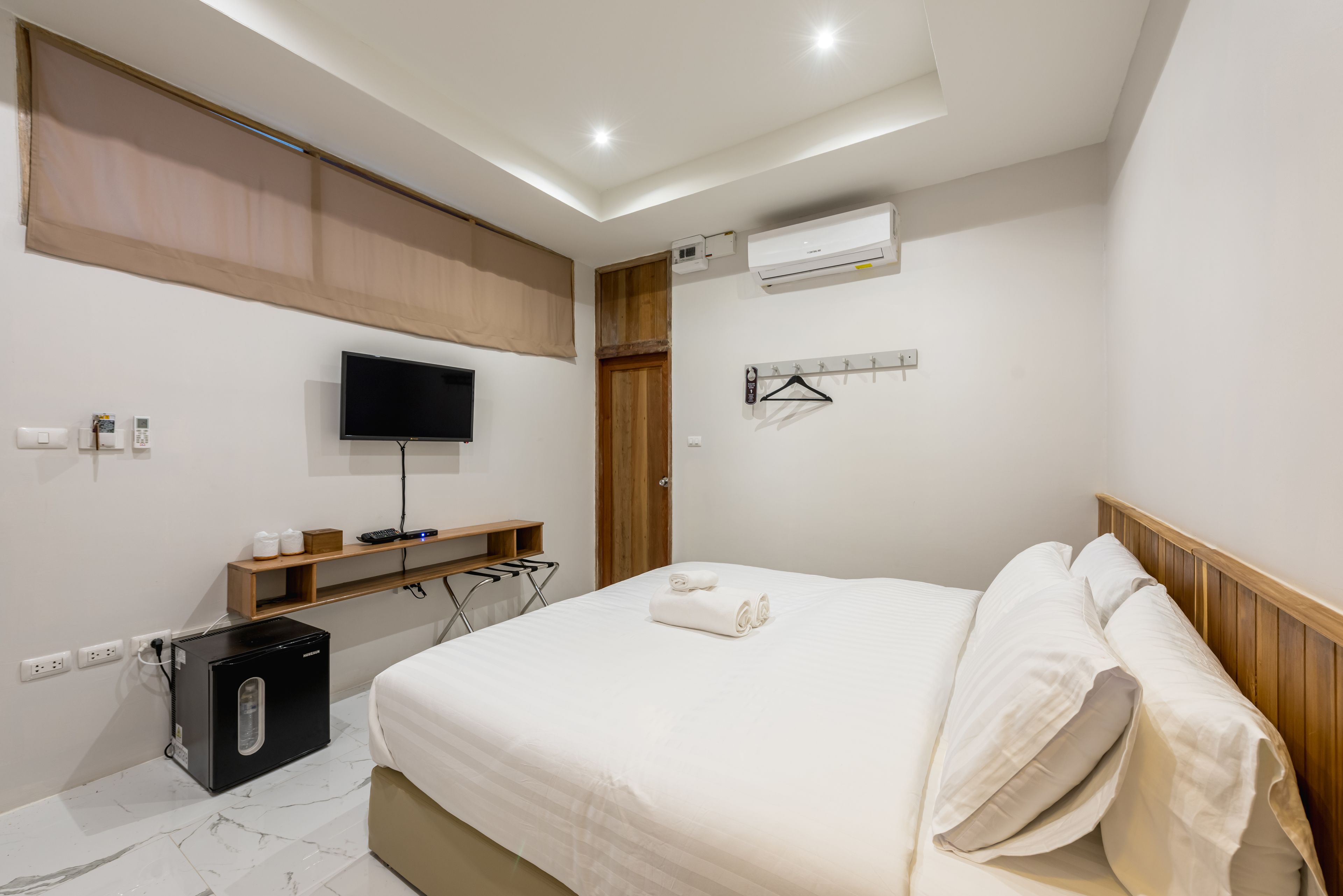 Une chambre d’hôtel moderne équipée d’un lit, d’une télévision, d’un mini-réfrigérateur et d’un porte-manteau.