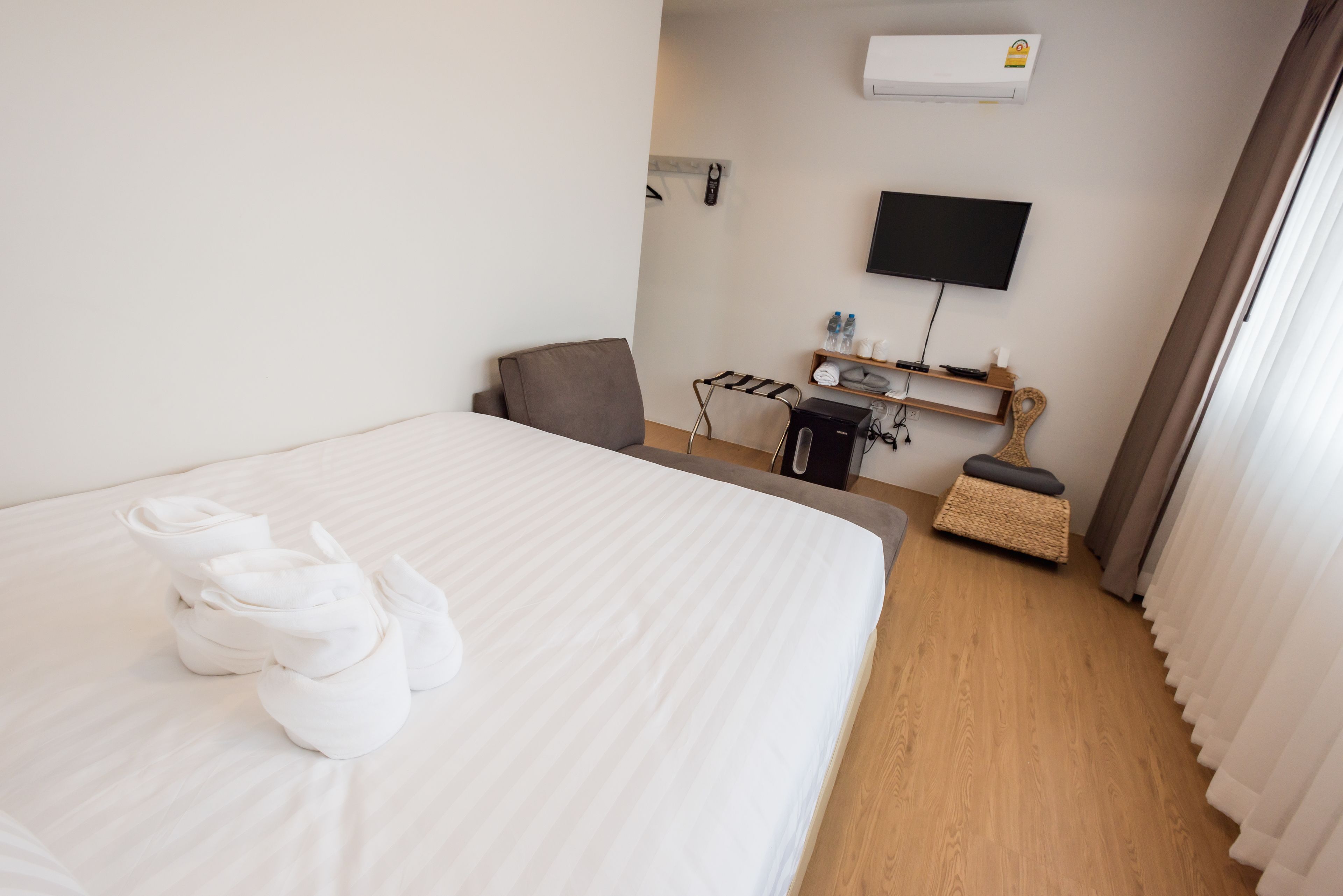 A hotel room with a neatly made bed, a TV mounted on the wall, a small seating area, and a shoe rack.