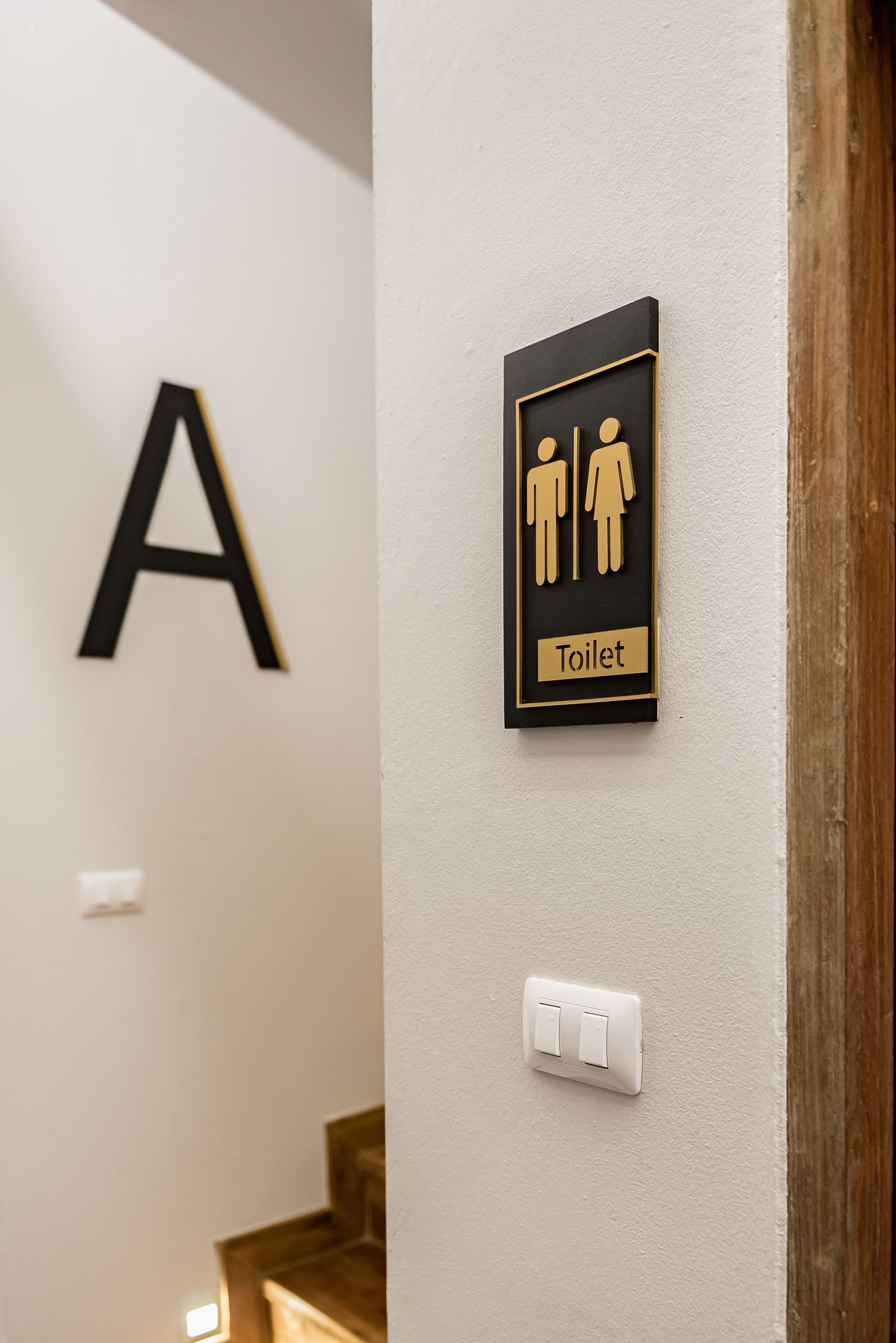 A wall-mounted sign indicating a toilet with a male and female symbol, a large capital letter 'A', and a light switch.