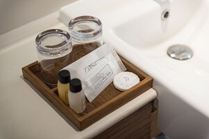 Una bandeja de madera con una botella, una vela y un recipiente pequeño sobre una encimera de baño.