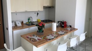 A kitchen with white cabinets, a wooden countertop, a sink, a stove, and a coffee maker. There are white chairs around the counter.