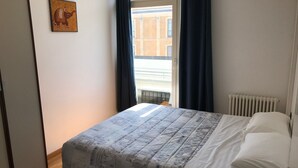 A bedroom with a bed, a window with curtains, a radiator, and a wall-mounted picture.