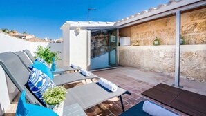 A rooftop terrace with lounge chairs, a table, and a glass door leading to a room. - House Ca na Serrieta in the village of Alcudia (Alcúdia)