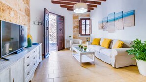 A living room with a television, white sofa with yellow cushions, a coffee table, and a potted plant. - House Ca na Serrieta in the village of Alcudia (Alcúdia)