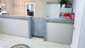 A reception desk with a modern design, a potted plant, and multiple flags on the counter. - Sky Hotel (Bishkek)