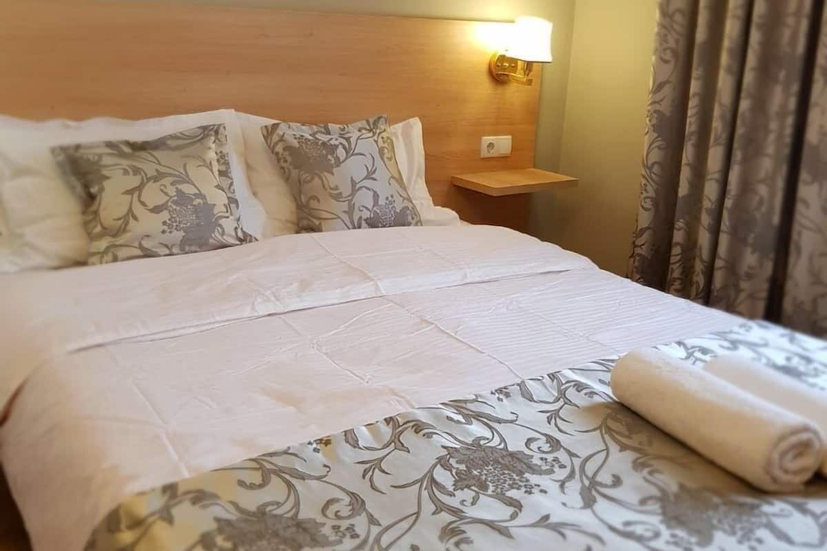 A neatly made bed with a floral-patterned bedspread and pillows, a bedside lamp, and a framed picture on the wall.