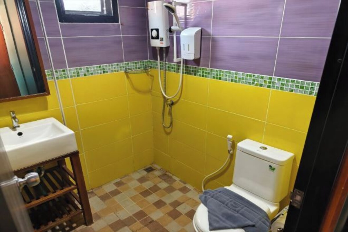 A small bathroom with yellow and purple tiles, a white sink, a toilet, and a shower.