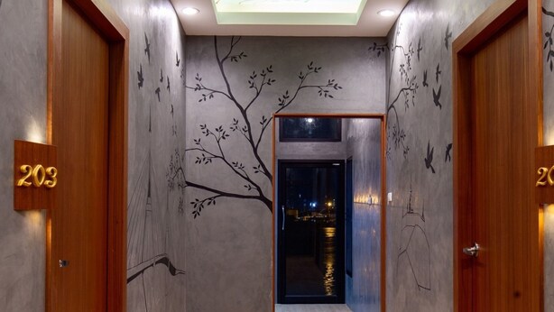 A hallway with a wooden floor, walls with bird and tree murals, and a ceiling with a bird mural. - Lilliput Riverside Bangkachao (Phra Pradaeng)