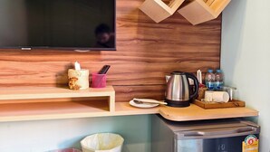 A modern kitchen with a built-in TV, wooden shelves, a coffee maker, and a mini-fridge. - Lilliput Riverside Bangkachao (Phra Pradaeng)