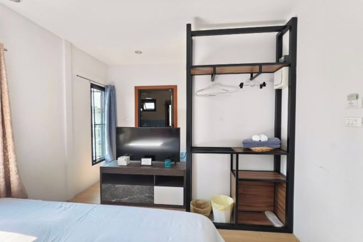 A hotel room with a bed, a TV, a desk with a computer, a shelf with towels, and a window with curtains.