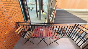 A balcony with a wooden table and chairs, a brick wall, and a view of the cityscape. - Lilliput Riverside Bangkachao (Phra Pradaeng)