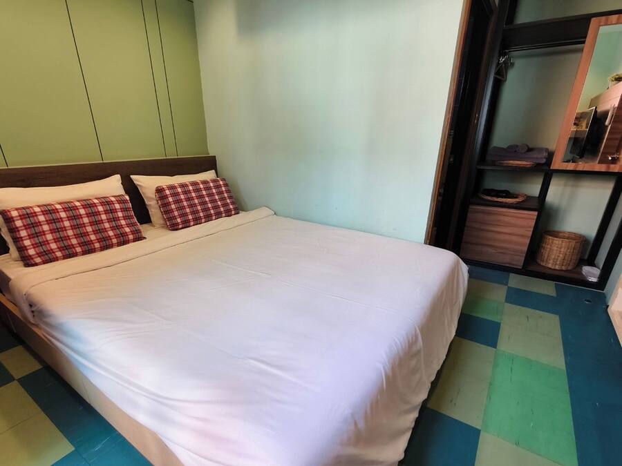 A bed with white bedding and plaid pillows, a checkered floor, and a mirror above a wooden shelf with items.