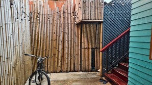 A bicycle parked against a bamboo fence in a residential area with a staircase leading to a green building. - Lilliput Riverside Bangkachao (Phra Pradaeng)