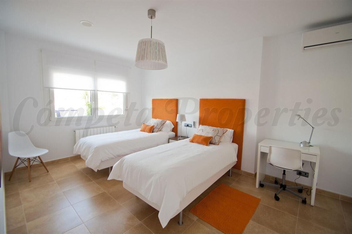 A bedroom with two beds, a desk, a chair, and a hanging light fixture.