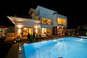 Une maison moderne à deux étages, dotée d’une piscine, de grandes fenêtres et d’un espace salon extérieur.
