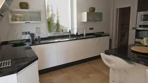 A modern kitchen with white cabinets, a black countertop, and a white bar stool. - New luxury villa, 5 bedrooms, 5 bathrooms, private pool (Canillas de Albaida)