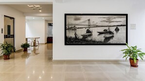 A hallway with a framed black and white painting of boats on water, potted plants, and a dining area with chairs and a table. - The Residency (Kolkata)