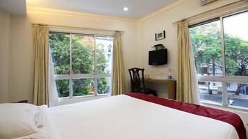 A hotel room with a bed, a desk with a chair, a TV, and large windows with curtains.