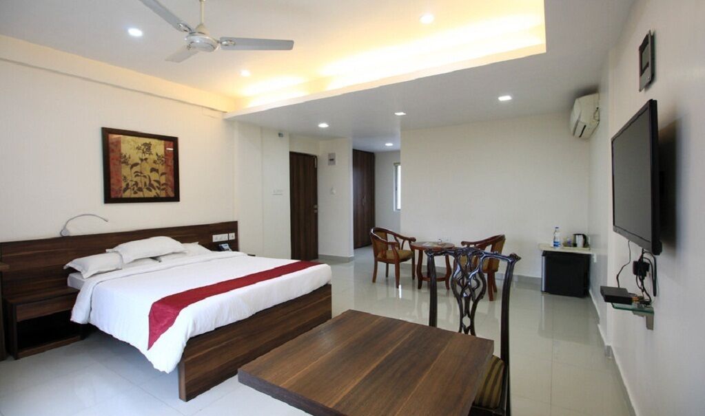 A hotel room with a bed, a dining table, chairs, a TV, and a ceiling fan.