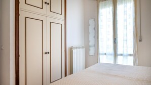 Un dormitorio con cama, armario, radiador y ventana con cortinas.