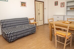 A room with a patterned sofa, wooden chairs, a dining table, and a cabinet.