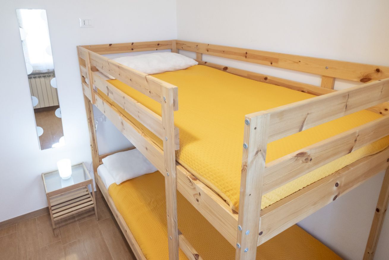 A bunk bed with a yellow mattress, a wooden frame, and a small bedside table with a white lamp.