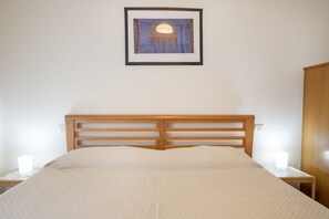 A neatly made bed with a wooden headboard, a framed artwork above it, and bedside lamps on either side.