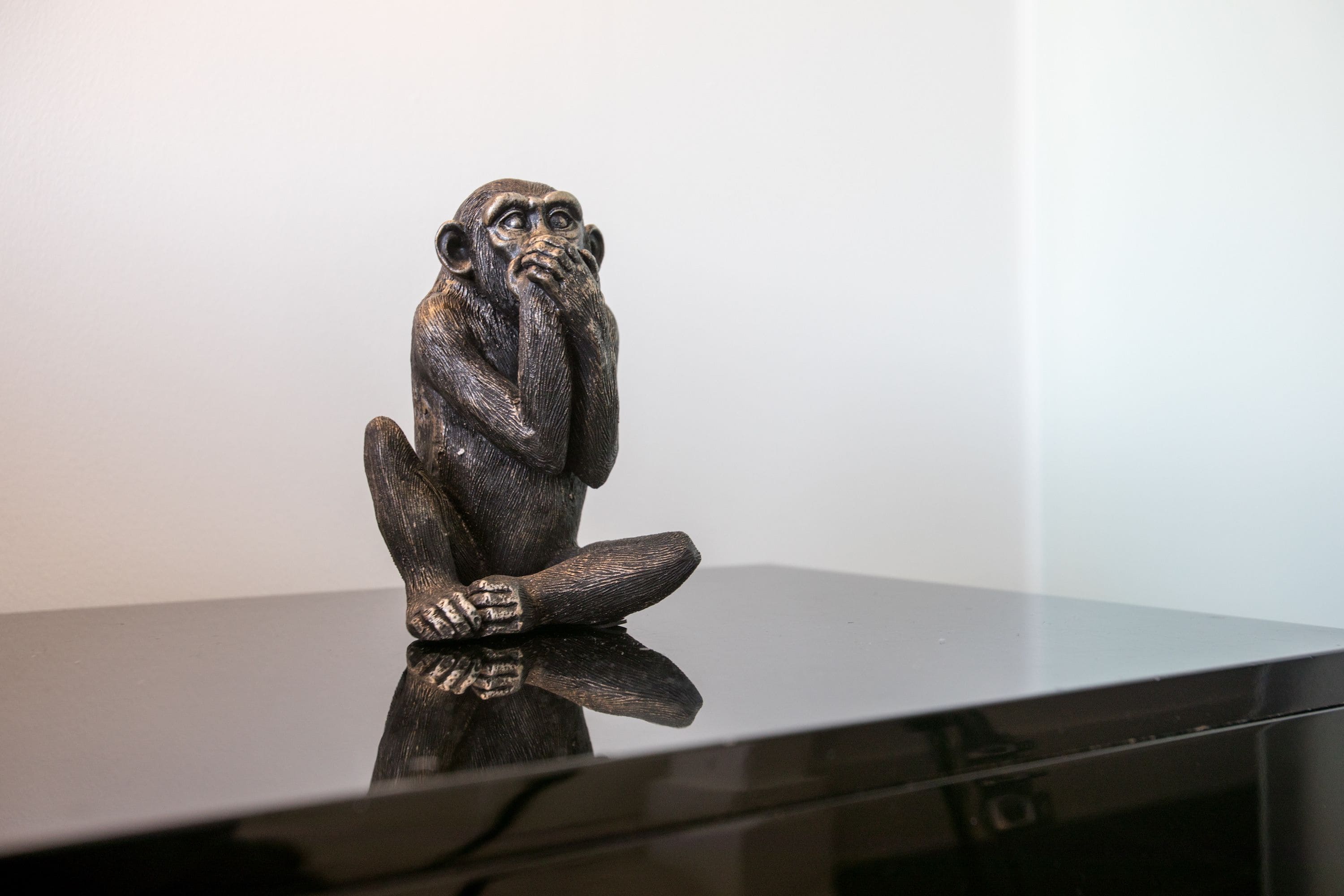 Escultura de uma figura sentada sobre uma superfície refletora.