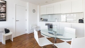 Una cocina moderna con armarios blancos, una mesa de comedor de vidrio y un reloj en la pared.