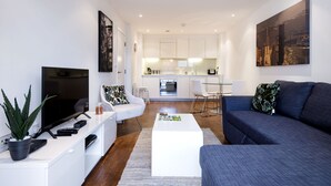 Una sala de estar moderna con un televisor de pantalla plana, una mesa de centro, un sofá y un comedor con una cocina al fondo.