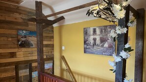 Een houten trap met een leuning, een gele muur en een schilderij van een straatbeeld.