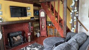 Een gezellige woonkamer met een open haard, een ruime bank, een houten trap en een flatscreen televisie aan de wand.