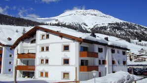 Ein mehrstöckiges Hotel mit verschneitem Dach, Holzbalkonen und einer Bergkulisse.