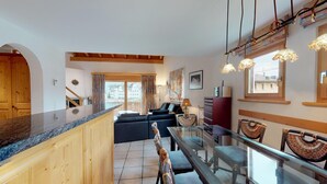 Eine moderne Küche mit Holzausstattung, ein Essbereich mit Glastisch und ein Wohnzimmer mit Sofa und Lampe.