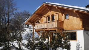 Un chalet en bois doté d’un balcon, entouré d’arbres et de montagnes couverts de neige.