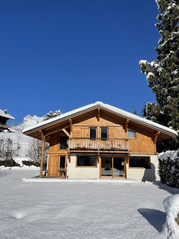 A wooden chalet with a balcony, large windows, and a snow-covered roof.