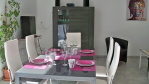 Un comedor con una mesa de vidrio dispuesta para cuatro personas, rodeado de sillas blancas.