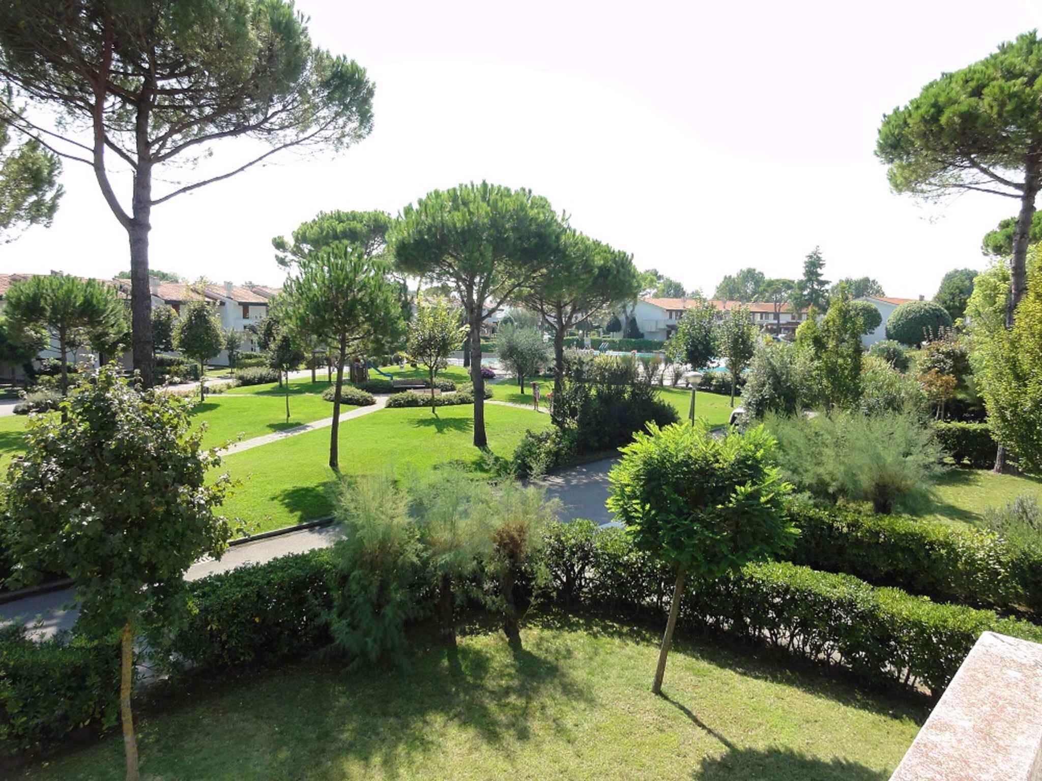 A well-maintained garden with various trees and shrubs, a clear pathway, and a view of residential buildings in the background.