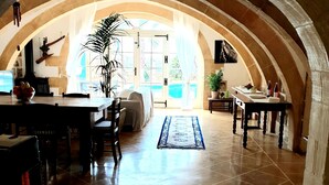 En matplats med ett välvt tak och utsikt över poolen, ett matbord dukat med tallrikar och glas, och en krukväxt.