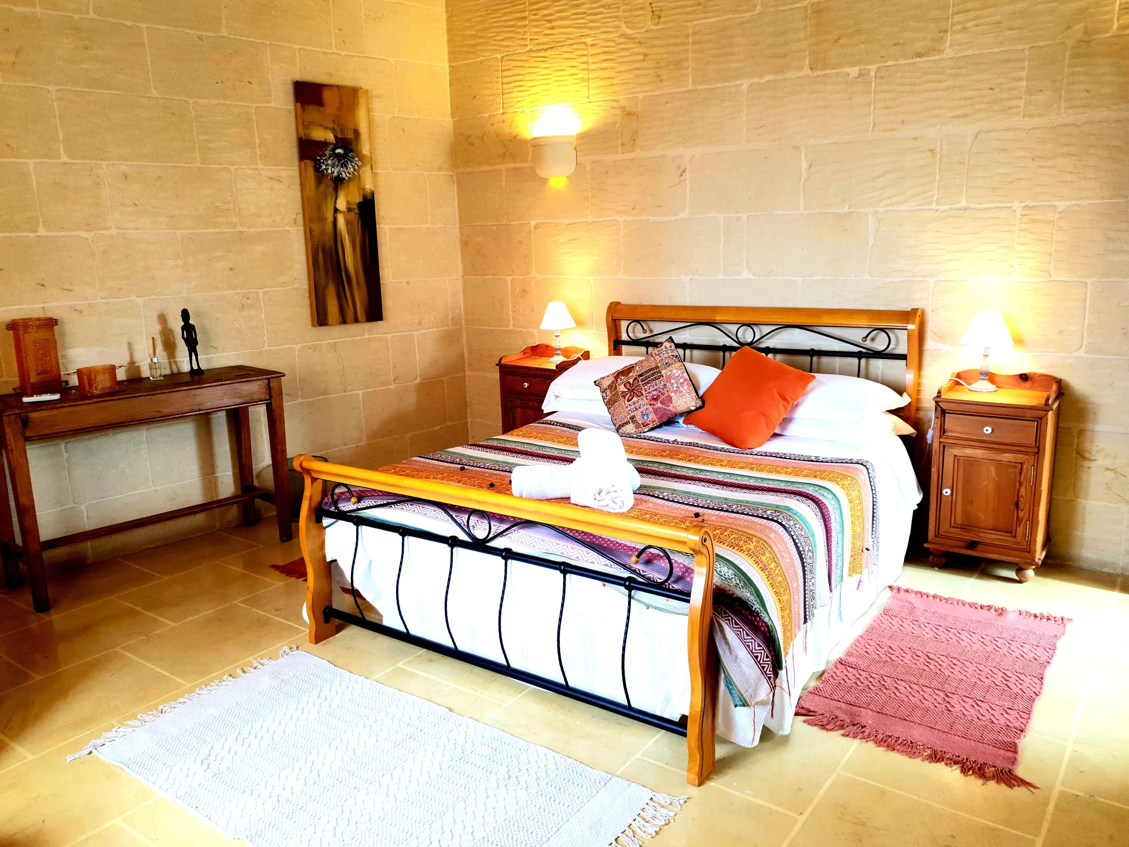 A bedroom with a bed, bedside tables, a nightstand, a wall-mounted lamp, and a small table with a lamp.