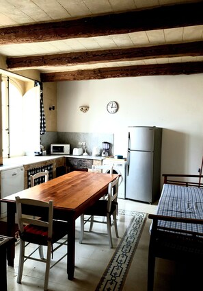 A compact kitchen with a wooden table, chairs, a refrigerator, a microwave, and a washing machine. - Panoramic Farmhouse (Gharb)