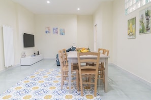 A dining area with a table and chairs, a sofa, and a television on the wall.