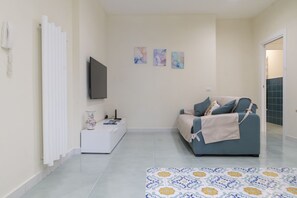 Un salon moderne avec un canapé, un téléviseur à écran plat, une petite table d’appoint blanche avec une lampe et un tapis à motifs.