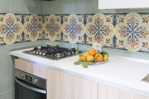Une cuisine équipée d’une cuisinière à gaz, d’un évier et d’un saladier rempli d’oranges posé sur le comptoir.