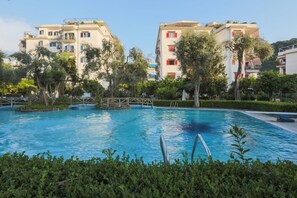 A swimming pool surrounded by lush greenery and modern buildings with balconies.