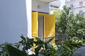 Un balcón con contraventanas amarillas, una pared blanca y una barandilla de metal.