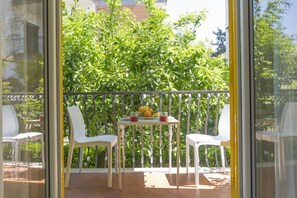 A balcony with two white chairs and a small table with fruit and a glass.
