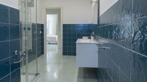 A modern bathroom with a glass shower enclosure, a white sink, and blue-tiled walls. - Modern Apartment with Terrace, Swimming Pool&Tennis (Sorrento)