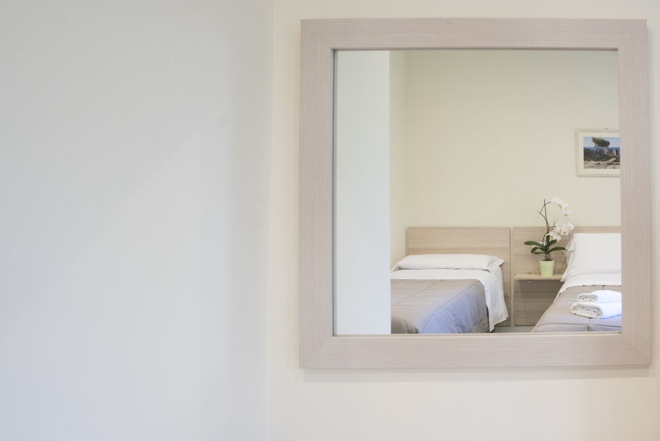 Ein Hotelzimmer mit zwei Betten, einem Nachttisch, einer Topfpflanze und einem gerahmten Bild an der Wand.