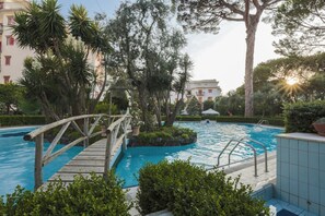 Un área de piscina con un puente de madera, rodeada de abundante vegetación y árboles.